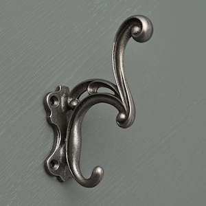 May include: A silver metal hook with a decorative scroll design. The hook is mounted on a wall.