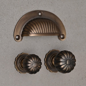 May include: Three antique brass cabinet knobs with a fluted design. The top knob is a pull handle with a curved shape.