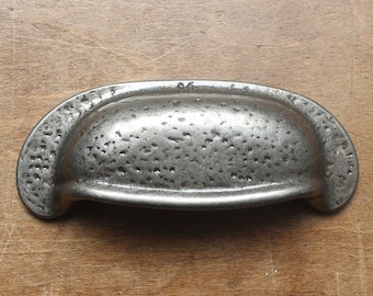 May include: A silver metal cabinet pull with a hammered finish. The pull is shaped like a half-circle and has a smooth, rounded edge.