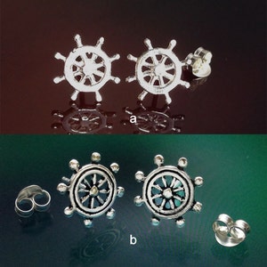 May include: Two pairs of silver ship wheel earrings. The first pair has a smooth silver finish. The second pair has a silver finish with a blue and green iridescent effect.