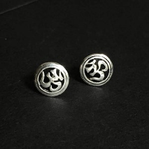 May include: A pair of silver stud earrings with a circular design featuring the Om symbol.