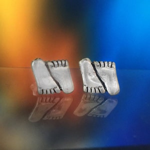May include: A pair of silver earrings shaped like footprints. The earrings are on a reflective surface.