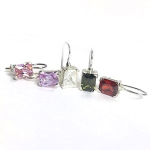 May include: Four pairs of silver earrings with different colored gemstones. The earrings feature a rectangular shaped gemstone with a silver setting. The gemstones are pink, clear, green, and red.