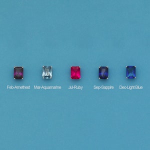 May include: Five square-shaped gemstones in different colors, arranged in a row. From left to right, the colors are purple, light blue, red, blue, and light blue.
