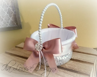 May include: A white and silver flower girl basket with a pearl handle and a blush pink satin bow. The basket is decorated with silver glitter and a rhinestone embellishment.
