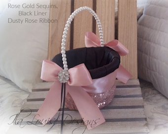 May include: A decorative basket with rose gold sequins, a black liner, and a dusty rose ribbon. The handle is adorned with pearls. The basket has a large bow and a rhinestone embellishment.