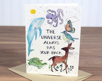 May include: Greeting card with watercolor illustrations of a whale, octopus, butterfly, bird, deer, and turtle. The card has the text "THE UNIVERSE ALWAYS HAS YOUR BACK" and is on a brown envelope.