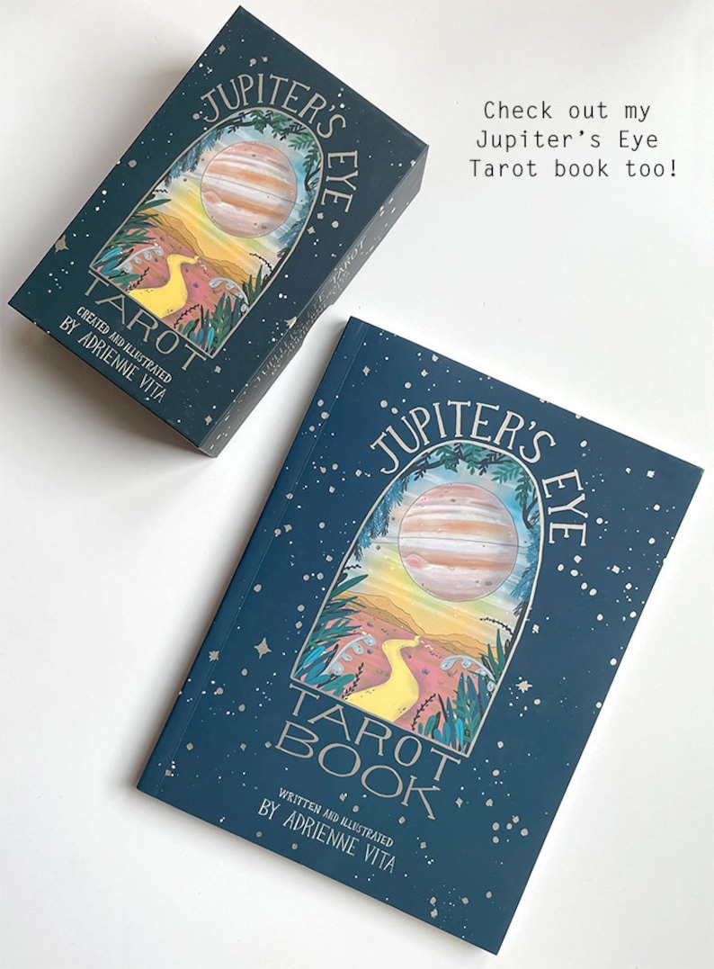 May include: Two blue and silver tarot decks with a Jupiter's Eye design. The top deck is a tarot deck and the bottom deck is a tarot book. Both decks feature a yellow path leading to a planet with a red and orange color scheme.