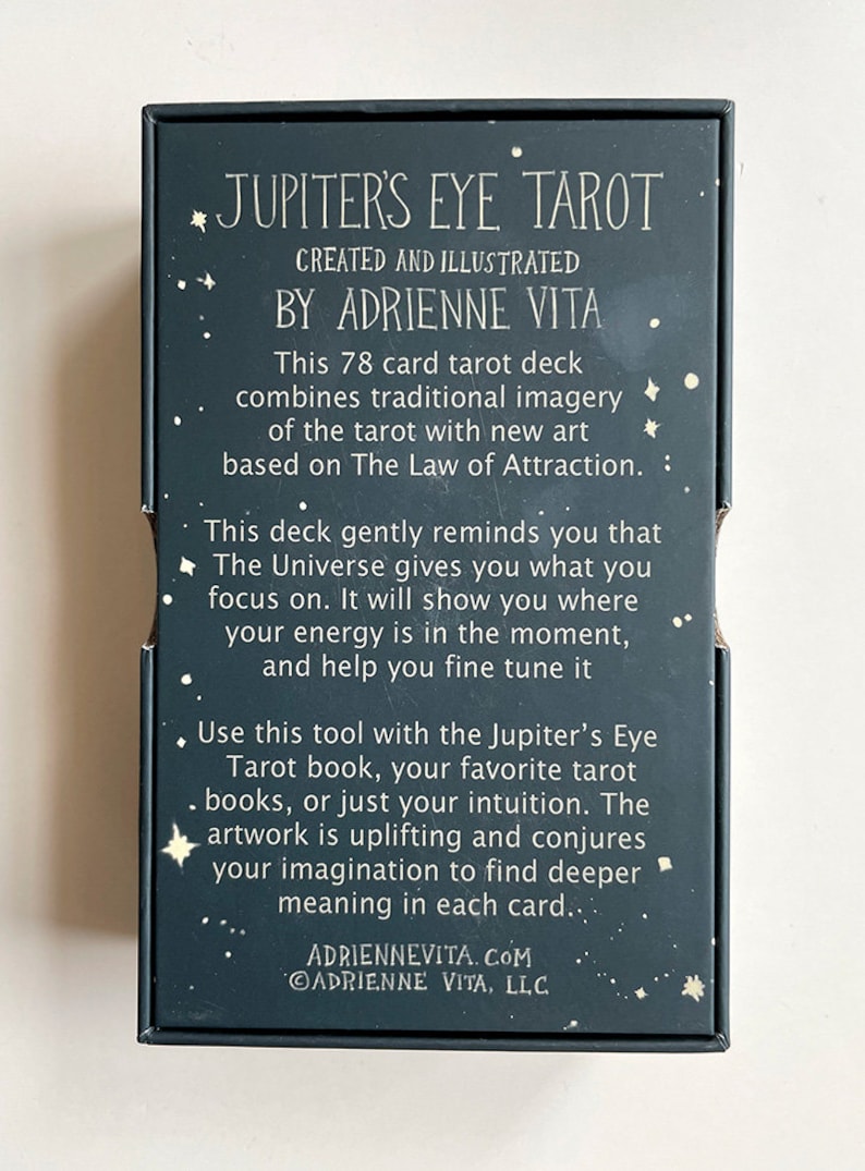 May include: A black box with a white border and gold stars. The box is for a 78 card tarot deck called "Jupiter's Eye Tarot" created and illustrated by Adrienne Vita. The text on the box describes the deck as combining traditional imagery of the tarot with new art based on the Law of Attraction.