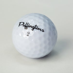 May include: A white golf ball with the text "Puffingtons 2" printed on it.