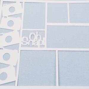 May include: White scrapbook paper with a cut-out design of cameras and the words "Oh Snap!"