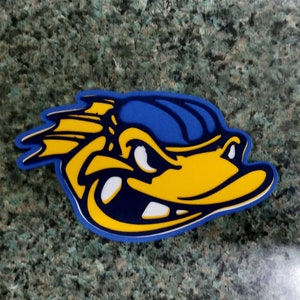 May include: A die-cut sticker featuring a stylized duck head in yellow, blue, and white. The duck has a determined expression, with a blue hat and a yellow beak. The sticker has a blue border and is likely a team logo or mascot.