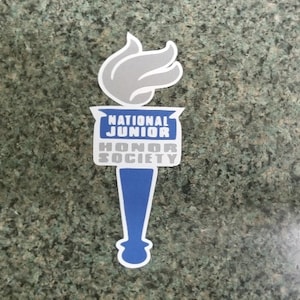 May include: A sticker featuring a torch design with the words "NATIONAL JUNIOR HONOR SOCIETY." The torch has a gray flame, a blue and white banner, and a blue handle. The sticker is white-bordered.