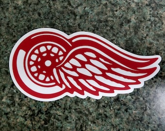 May include: Red and white Detroit Red Wings logo sticker. The logo features a stylized wing with a wheel inside.