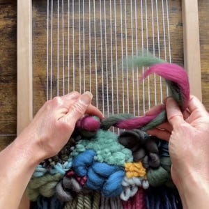 Puede incluir: Primer plano de un telar con un tapiz tejido de colores. El tapiz está hecho con varios tonos de azul, verde, rojo y amarillo. La lana está tejida en una variedad de texturas y patrones. El telar está hecho de madera y tiene un hilo de urdimbre blanco.