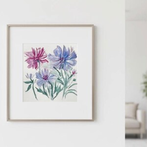 Puede incluir: Pintura a la acuarela de flores azules y moradas con hojas verdes. La obra de arte est&aacute; enmarcada en un marco gris claro con un passe-partout blanco. La pintura se exhibe en una pared blanca.