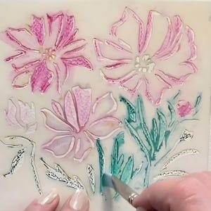 Puede incluir: Primer plano de un dise&ntilde;o de plantilla floral con pintura de acuarela rosa y verde. La plantilla presenta varios contornos de flores y hojas. Una mano sostiene un pincel, aplicando la pintura verde a las hojas.