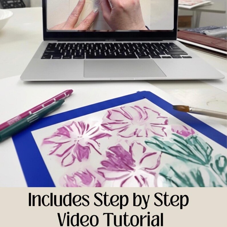 Puede incluir: Un port&aacute;til muestra un tutorial en v&iacute;deo. Debajo, una alfombrilla azul contiene una pintura floral con acentos morados y verdes. Tambi&eacute;n se ven dos rotuladores y un pincel. El texto "Includes Step by Step Video Tutorial" est&aacute; en la parte inferior.