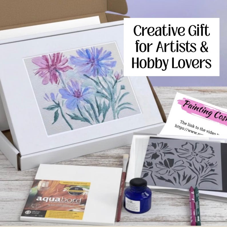 Puede incluir: Un juego de arte en una caja blanca, que contiene una pintura en acuarela enmarcada de flores moradas y azules. El juego incluye una botella de tinta azul, pinceles y una plantilla. La caja tiene texto que dice "Creative Gift for Artists & Hobby Lovers."