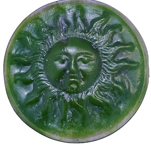May include: A green ceramic sun with a face and rays. The sun is a decorative wall hanging.