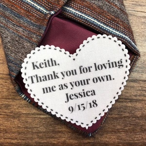 May include: A white heart-shaped card with the text "Keith. Thank you for loving me as your own. Jessica 9/15/18" on a striped tie.