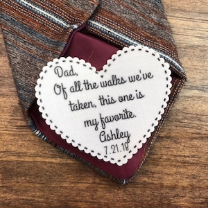 May include: A white heart-shaped tag with a scalloped edge, attached to a brown and blue striped tie. The tag has the text "Dad, Of all the walks we've taken, this one is my favorite. Ashley 7.21.18" embroidered on it.