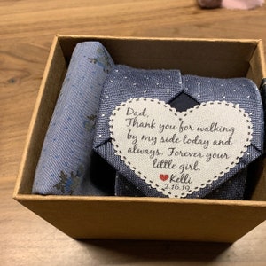 May include: A blue tie with a white polka dot pattern and a heart-shaped tag attached. The tag has a handwritten message that reads: "Dad, Thank you for walking by my side today and always. Forever your little girl. Kelli 2.16.19"
