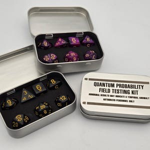 Puede incluir: Dos latas de metal plateadas que contienen juegos de dados. La lata superior tiene un juego de dados de mármol morado y negro con números dorados. La lata inferior tiene un juego de dados negros con números dorados. La lata inferior tiene una etiqueta que dice "Quantum Probability Field Testing Kit. Abnormal results may indicate a temporal anomaly. Authorized personnel only."