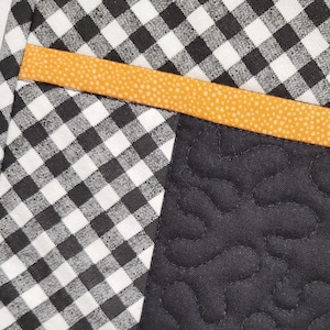 May include: A black and white checkered fabric with a bright orange trim. The fabric is sewn together with a black fabric with a quilted pattern.