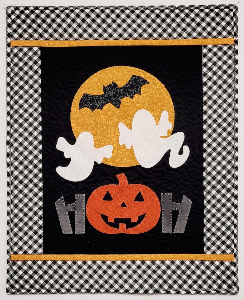 May include: A black and white checkered fabric with a black panel featuring a yellow moon with a bat, two white ghosts, a large orange pumpkin with a jack-o-lantern face, and the word "HOH" in gray.
