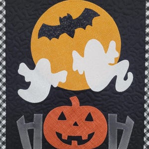May include: A black and white quilted Halloween banner with a yellow moon, a bat, two ghosts, a pumpkin, and the word "BOO" in gray letters.