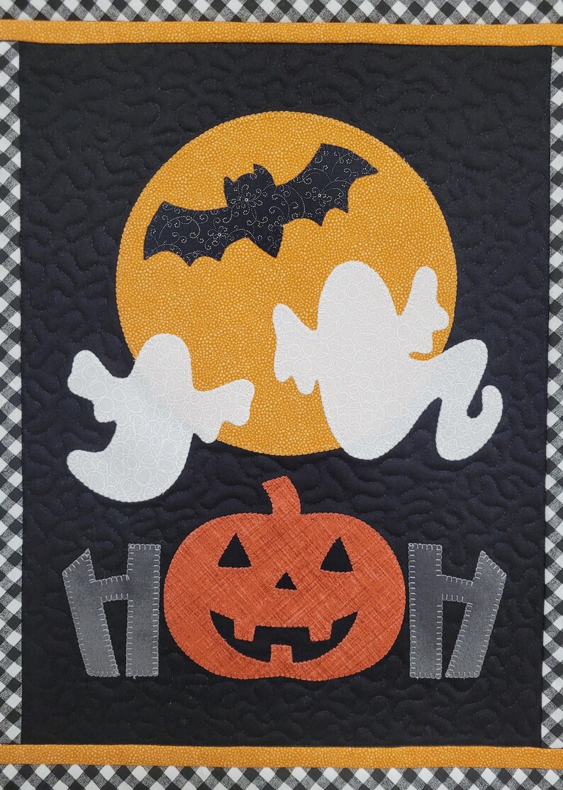 May include: A black and white quilted Halloween banner with a yellow moon, a bat, two ghosts, a pumpkin, and the word "BOO" in gray letters.