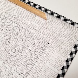 May include: A black and white checkered fabric frame with a wooden dowel. The fabric is wrapped around a piece of paper with a black and white design of a maze.