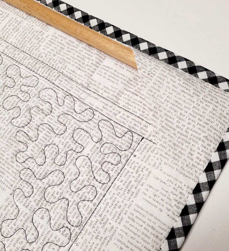 May include: A black and white checkered fabric frame with a wooden dowel. The fabric is wrapped around a piece of paper with a black and white design of a maze.