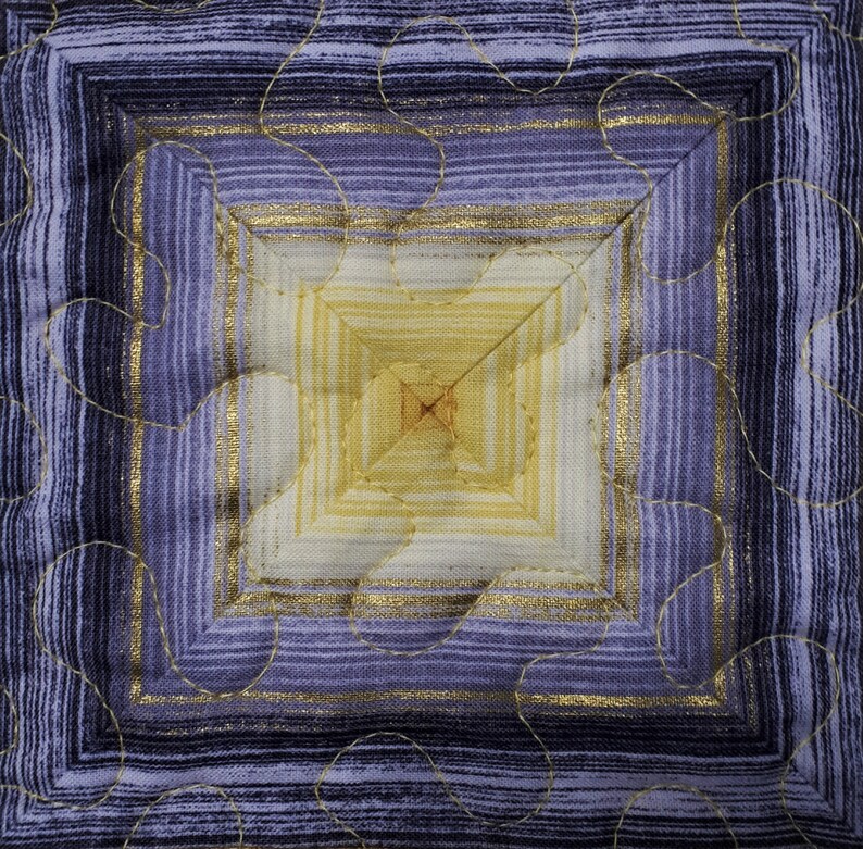 May include: A square quilted fabric with a concentric pattern of gold and purple stripes. The center of the square is a lighter shade of yellow.