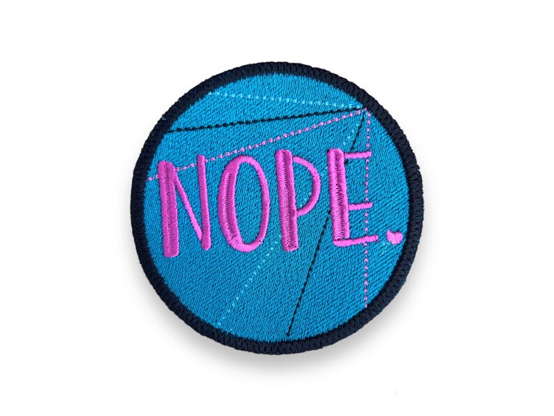 K&ouml;nnte beinhalten: Runder, gestickter Aufn&auml;her mit dem Wort "NOPE" in rosa Schrift. Der Aufn&auml;her hat einen t&uuml;rkisblauen Hintergrund mit einem geometrischen Design und einem schwarzen Rand. Ein lustiges Accessoire f&uuml;r Jacken, Taschen oder H&uuml;te.