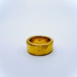May include: A thick gold band ring with a textured surface.