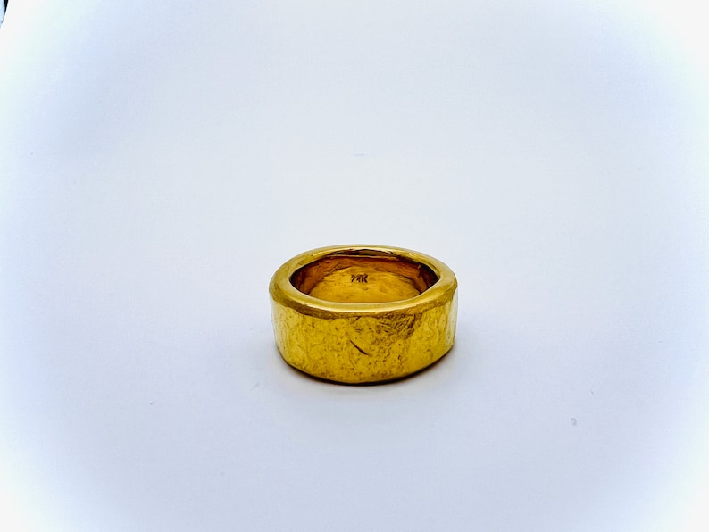 May include: A thick gold band ring with a textured surface.