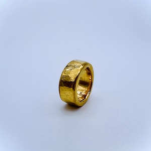 May include: A gold ring with a textured, hammered finish. The ring is thick and has a wide band.