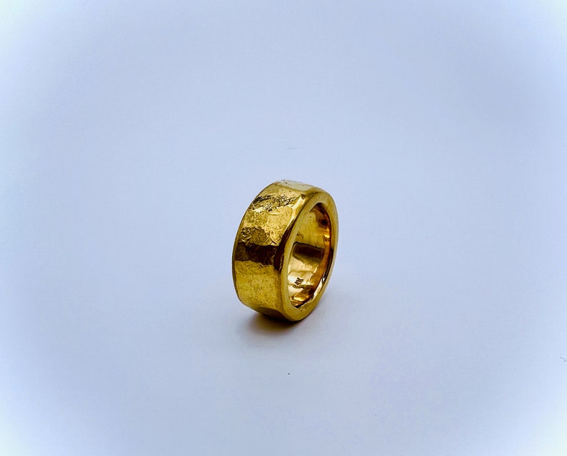 May include: A gold ring with a textured, hammered finish. The ring is thick and has a wide band.