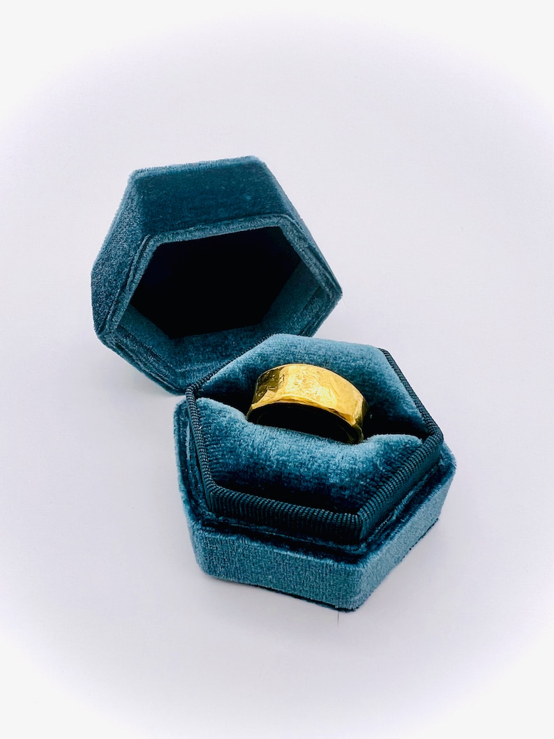 May include: A gold ring with a textured surface sits inside a teal velvet ring box.