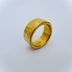 May include: A gold band ring with a hammered texture. The ring is thick and has a polished inner band.