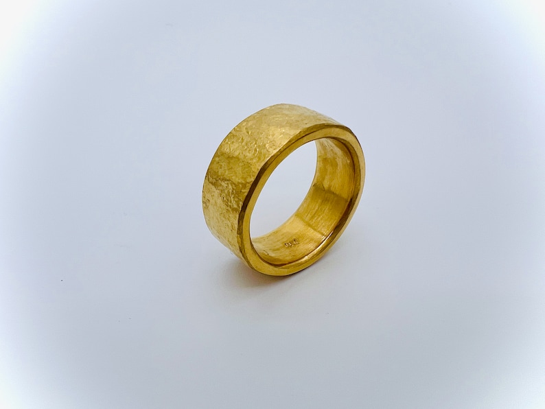May include: A gold band ring with a hammered texture. The ring is thick and has a polished inner band.