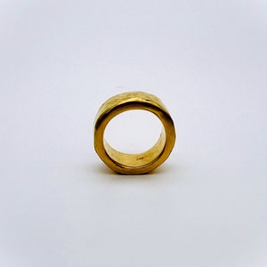 May include: A gold ring with a hammered texture. The ring is thick and has a wide band.