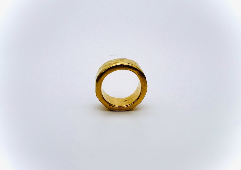 May include: A gold ring with a hammered texture. The ring is thick and has a wide band.