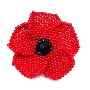 May include: A handcrafted red beaded poppy flower brooch with a black center. The brooch is made of small, round red beads, meticulously arranged to form the petals. The center features a cluster of black beads.