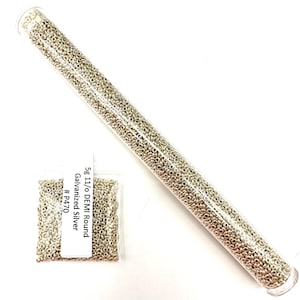 May include: A clear tube and a small bag filled with small, silver-colored beads. The tube is filled with beads, and the bag has a label that reads "5g 11/o DEMI Round Galvanized Silver #P470". The beads appear to be for jewelry making.