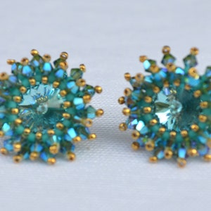 May include: A pair of blue and gold earrings with a starburst design. The earrings are made with small, faceted beads and a larger, clear crystal in the center.
