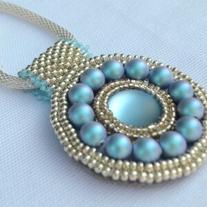 May include: A silver chain necklace with a pendant featuring a light blue iridescent stone surrounded by a circle of smaller light blue iridescent beads.