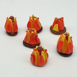 May include: Six handmade glass flower beads in shades of red, orange, and yellow. Each bead has a dark brown base and a small, dark red center. The beads are arranged on a white surface.